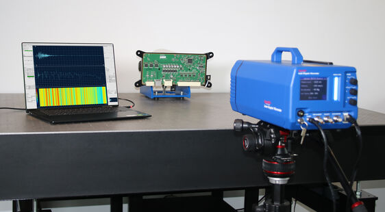 Ein Laser-Doppler-Vibrometer wird auf ein elektronisches Bauteil gerichtet, während die Schwingungsdaten in Echtzeit auf einem Laptop visualisiert werden. Die Messung erfasst präzise die Bewegungen und Vibrationen der Leiterplatte, um ihre strukturelle Integrität zu überprüfen. Der Aufbau demonstriert die Kombination aus moderner optischer Messtechnik und Datenanalyse.